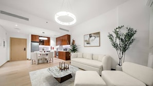 A modern living room with a sofa, coffee table, and dining area. - Luxury La Mer 1BR | Balcony Sea Views + Near City Walk & Mall (Dubai)
