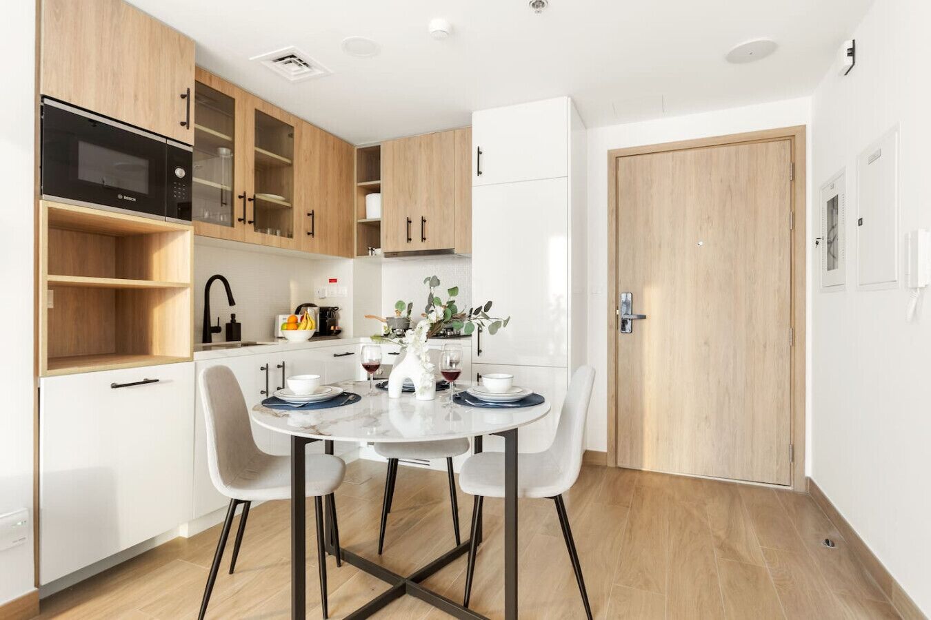 A modern kitchen with a built-in microwave, wooden cabinets, and a dining area with a round table and chairs.