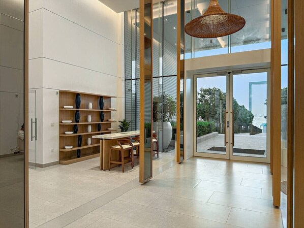 A modern interior with a glass door leading to a balcony, a wooden table with chairs, and shelves with decorative items.