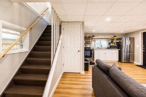 A staircase leading to a kitchen with modern appliances, a sofa in the living area, and a door to another room.
