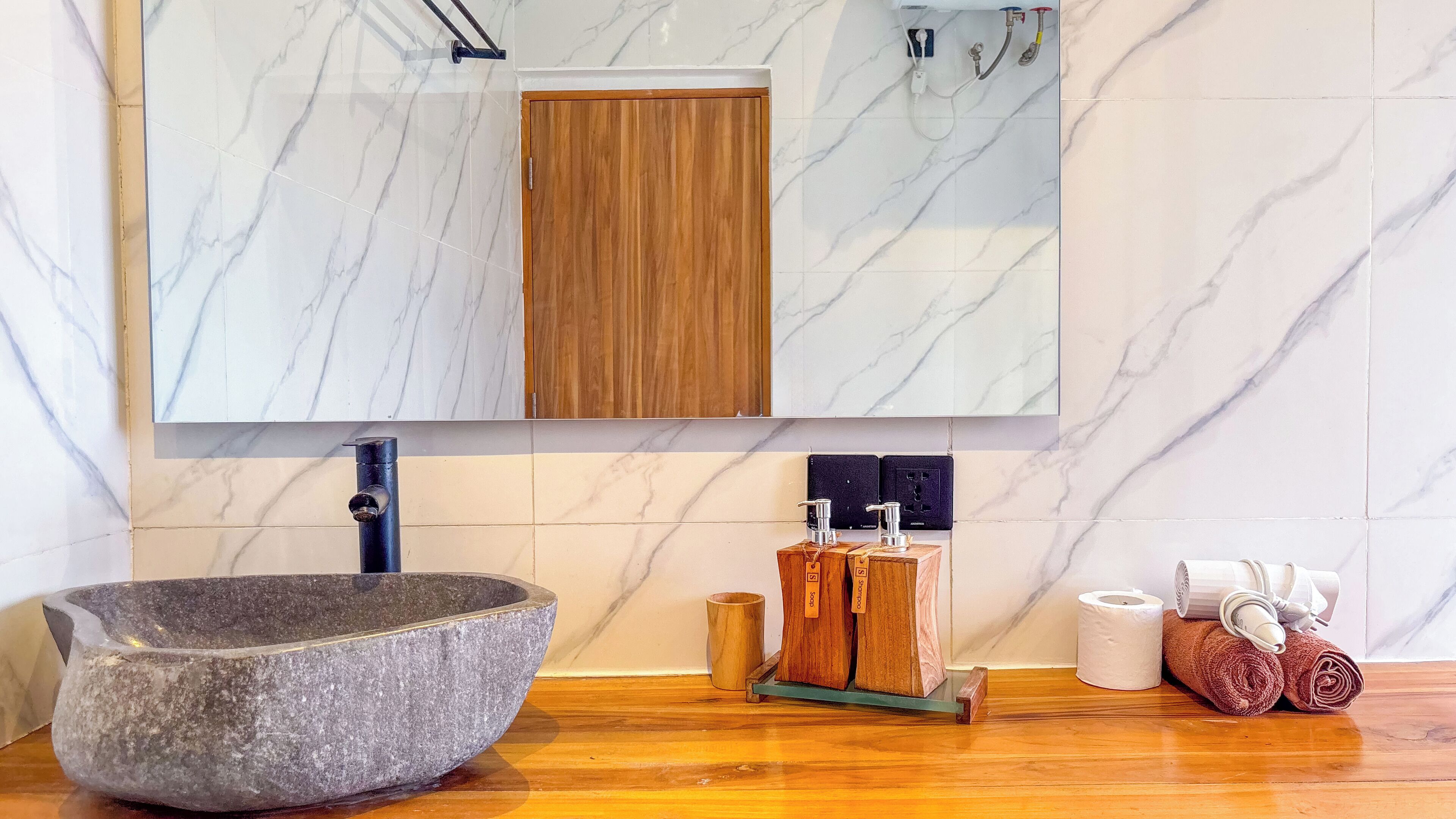 A bathroom with a stone basin, wooden soap holders, and a mirror above a wooden door.