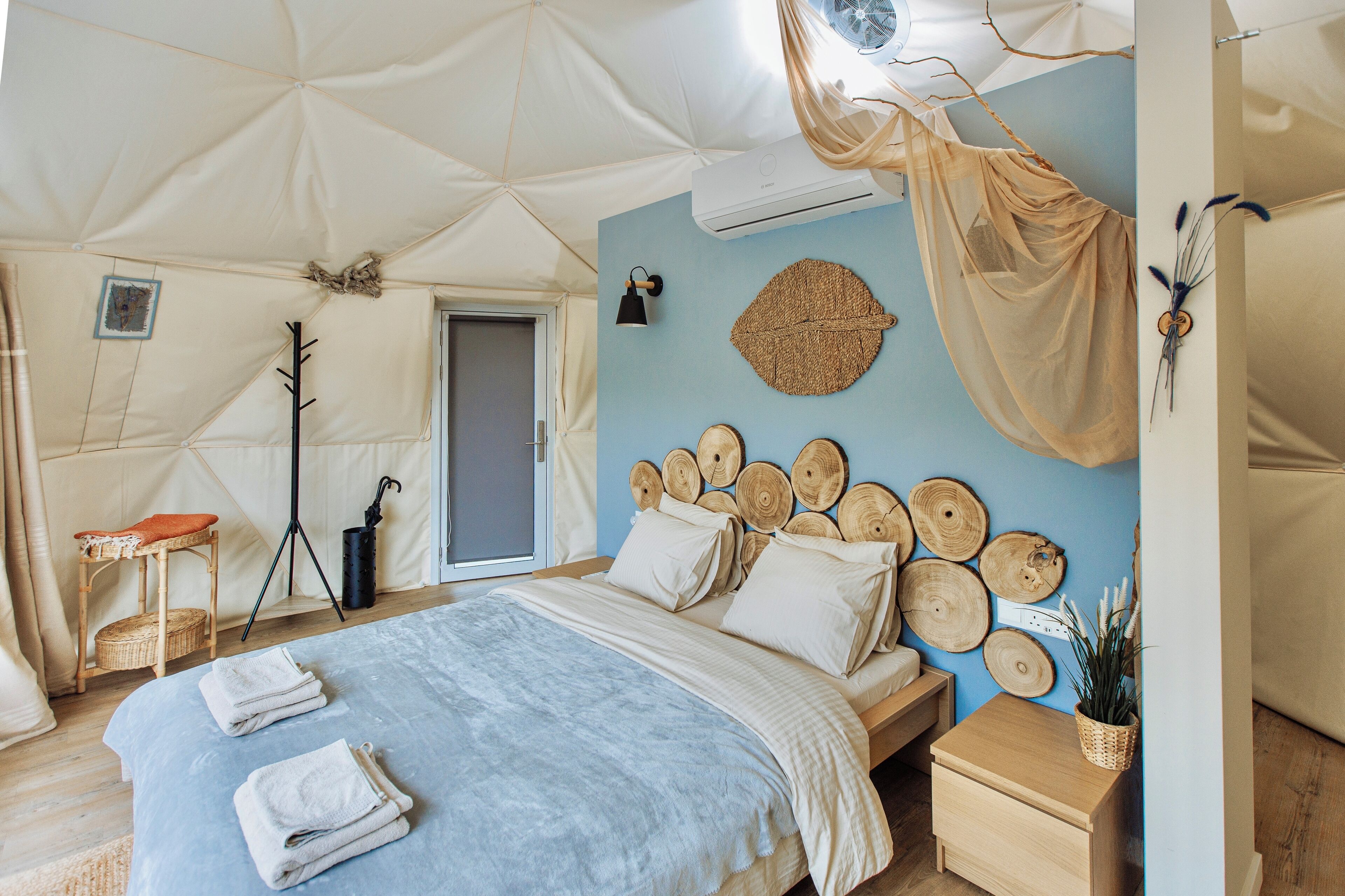 A tented room with a bed, bedside table, and a wall decorated with wooden slices.