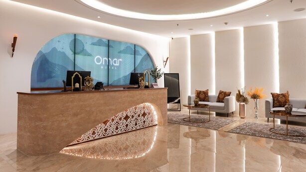 A modern hotel lobby with a reception desk, seating area, and a large digital display. - Omar Hotel (Tangerang)