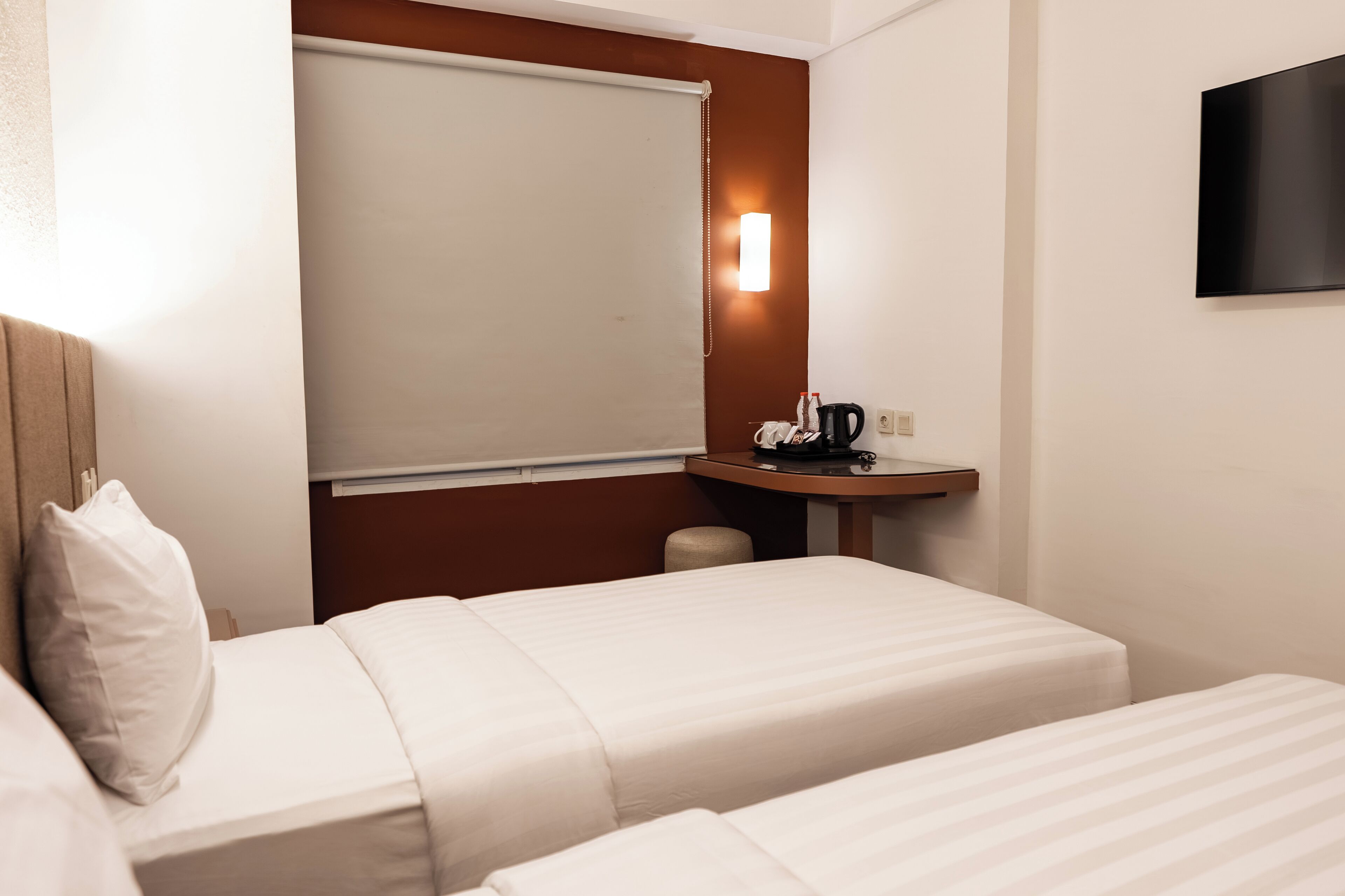 Ein Hotelzimmer mit zwei Betten, einem kleinen Schreibtisch mit Telefon und Lampe sowie einem Wand-Fernseher.