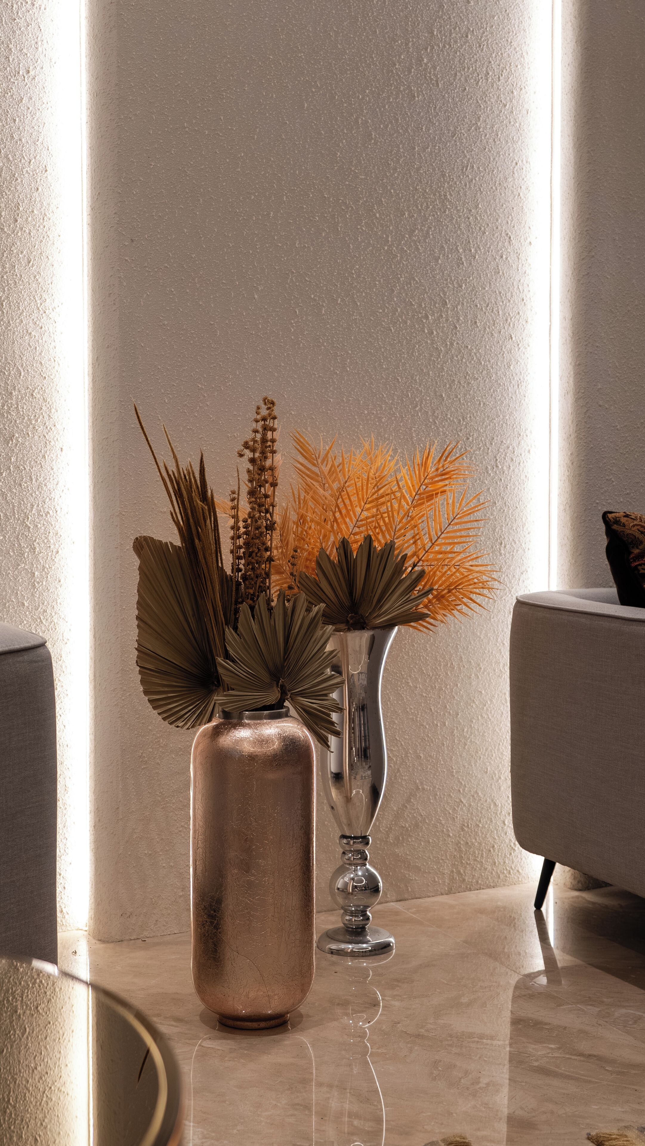 A modern interior with two vases on a marble table, one with dried plants and the other with a metallic finish.