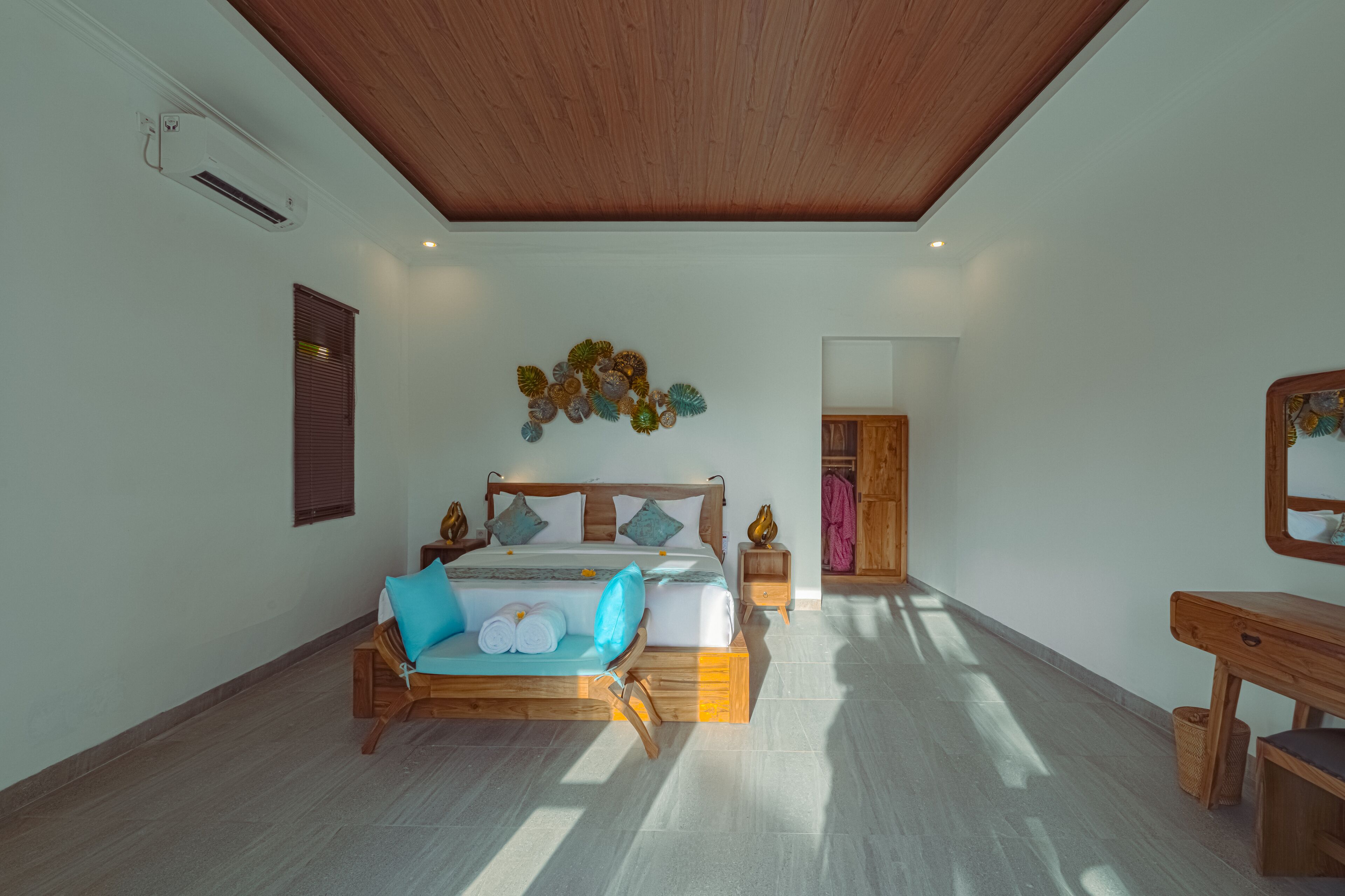 A bedroom with a wooden ceiling, a bed with blue and white bedding, a wooden bench, a nightstand, and a wall-mounted mirror.