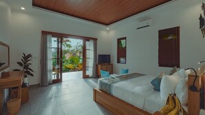 A modern bedroom with a large bed, a TV, and a desk. There is a sliding glass door leading to a balcony with plants. - Matahari Lumbung Resort (Ubud)