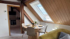 A dining area with a round table, chairs, and a bottle of champagne. - Vineyard View Attic Suite (Ruppertsberg)