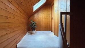A small, wooden room with a sloped ceiling and a skylight. There is a potted plant on a flat surface and a door on the right side. - Vineyard View Attic Suite (Ruppertsberg)