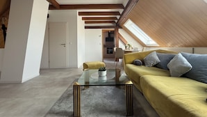 A modern loft with exposed wooden beams, a glass coffee table, a yellow sofa, and a skylight. - Vineyard View Attic Suite (Ruppertsberg)