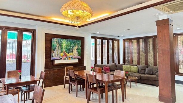 A spacious living area with a dining table, chairs, a sofa, and a large TV screen.
