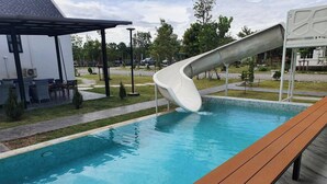 Una piscina con tobogán, rodeada por una terraza y mobiliario de exterior.