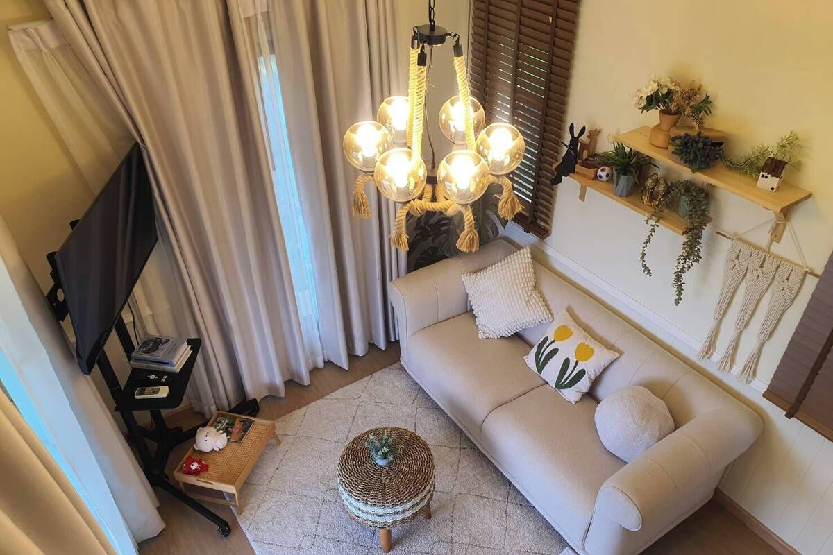 A cozy living room with a sofa, a round ottoman, a coffee table, a bookshelf, and a hanging light fixture.