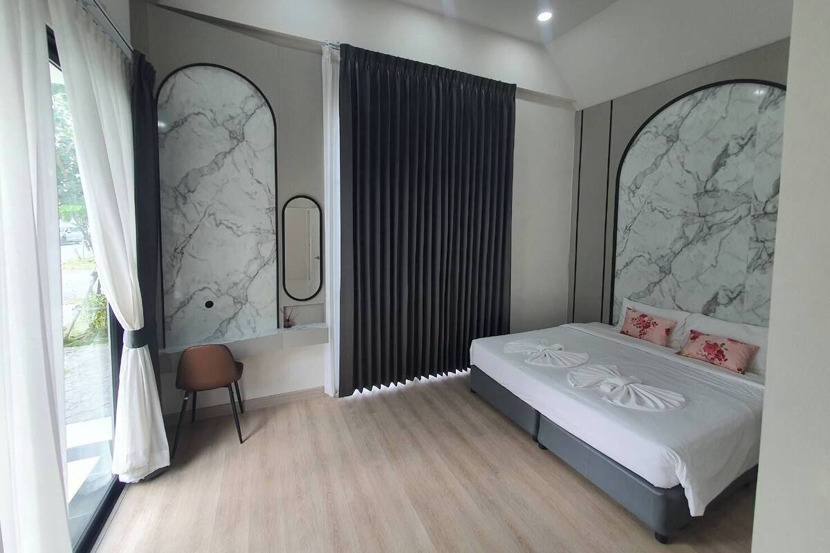 A modern bedroom with a bed, a chair, a mirror, and a window with curtains.
