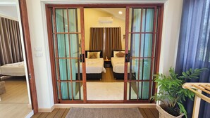 Habitación de hotel con puerta corrediza de vidrio que da a un balcón, una cama con cabecera, una mesita de noche y una planta en maceta.