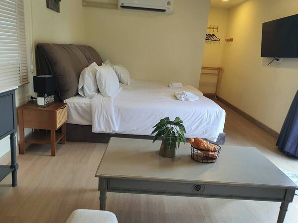 Une chambre d’hôtel avec un lit, une table de chevet avec une lampe, une petite table avec une plante et du pain, et un téléviseur fixé au mur.