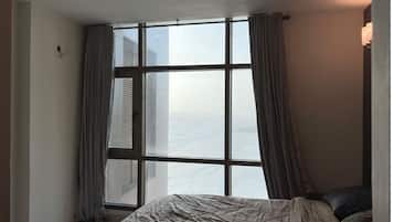 A hotel room with a large window, a bed, a ceiling fan, and a nightstand with a lamp.