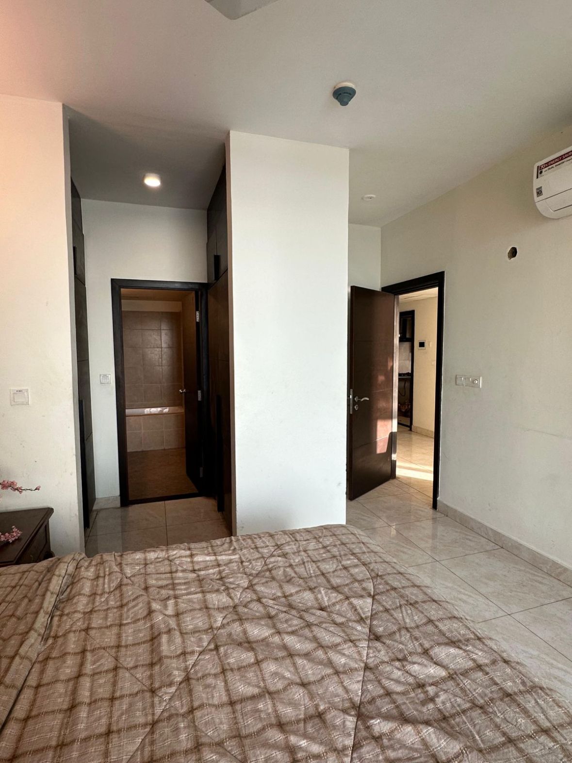 A room with a bed, a door leading to another room, and a ceiling-mounted air conditioning unit.