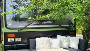 A green bus with a black interior, featuring a sofa with white cushions and a fur throw. - Luxury tiny house with sauna in Lierneux (Lierneux)