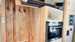 A compact kitchen with a built-in oven, a wooden wall, and a small countertop. - Luxury tiny house with sauna in Lierneux (Lierneux)