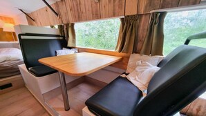 A compact, well-lit interior with a wooden panel wall, a small table, and seating area with cushions. - Luxury tiny house with sauna in Lierneux (Lierneux)