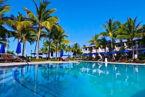 A pool area with palm trees, lounge chairs, and umbrellas.