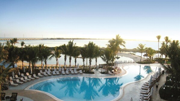 A resort pool with lounge chairs and palm trees, overlooking a beach and water.