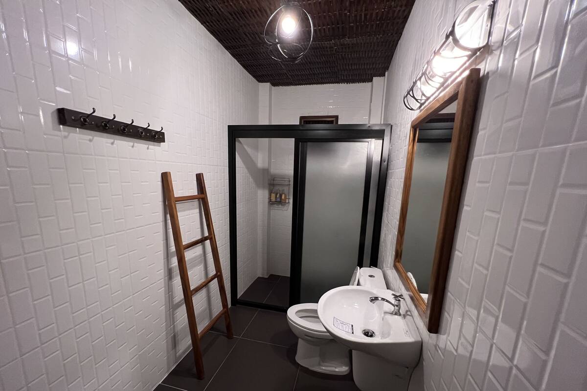 Bany amb parets de rajola blanca, escala de fusta, vàter i un lavabo amb mirall.