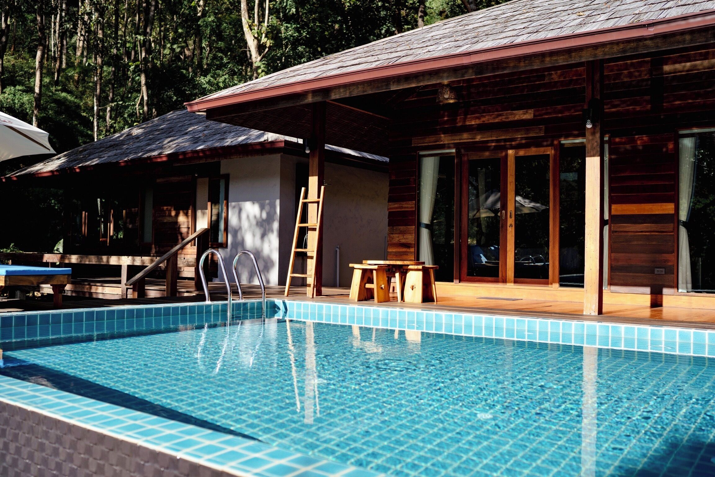 Une piscine avec une terrasse en bois et un espace salon abrité.
