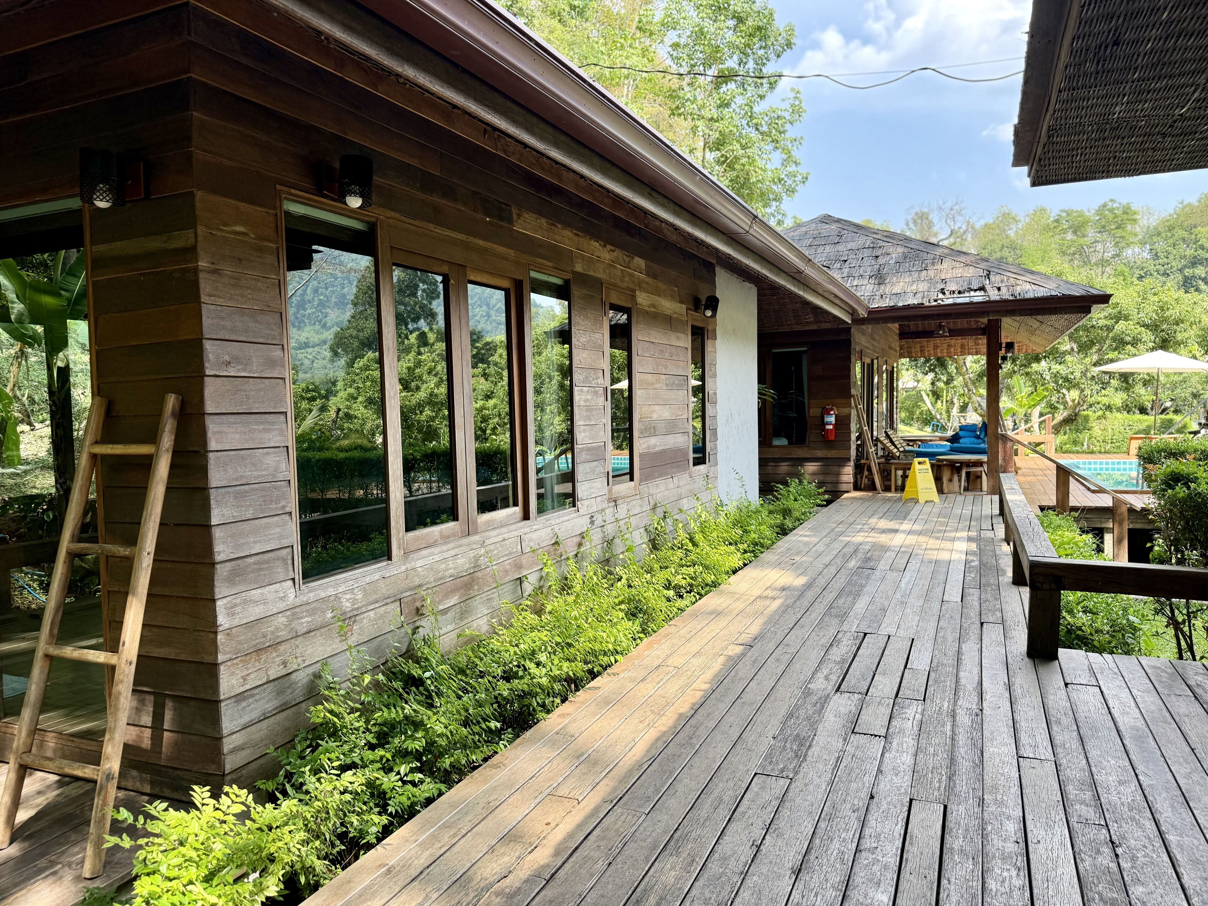 Una terraza de madera con piscina, un espacio de estar techado y una escalera de madera.