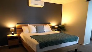 A modern bedroom with a wooden bed, bedside lamps, and a wall-mounted air conditioner. - Spacious Retreat, Walk to Town (Denman)