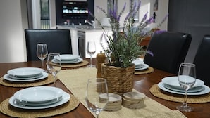 A dining area with a wooden table set for four, surrounded by chairs. A woven placemat runs along the table's length, and a woven basket with lavender plants is placed in the center. - Spacious Retreat, Walk to Town (Denman)