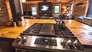 A kitchen with a stainless steel stove, a digital clock displaying 75.7, and a wooden interior. - The Overlook/Cozy 2 bed/Hot Tub/Wood Stove/Firepit (Carroll County)