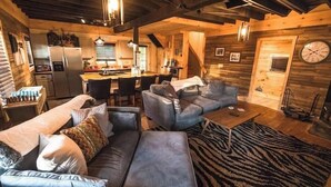 A cozy cabin interior with a living area featuring a sofa, a coffee table, and a rug. There is a kitchen area with a refrigerator and a dining table. - The Overlook/Cozy 2 bed/Hot Tub/Wood Stove/Firepit (Carroll County)