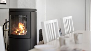A modern wood-burning stove with a glass door, white chairs, and a table with a magazine.