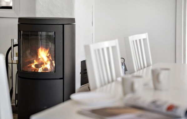 A modern wood-burning stove with a glass door, white chairs, and a table with a magazine.