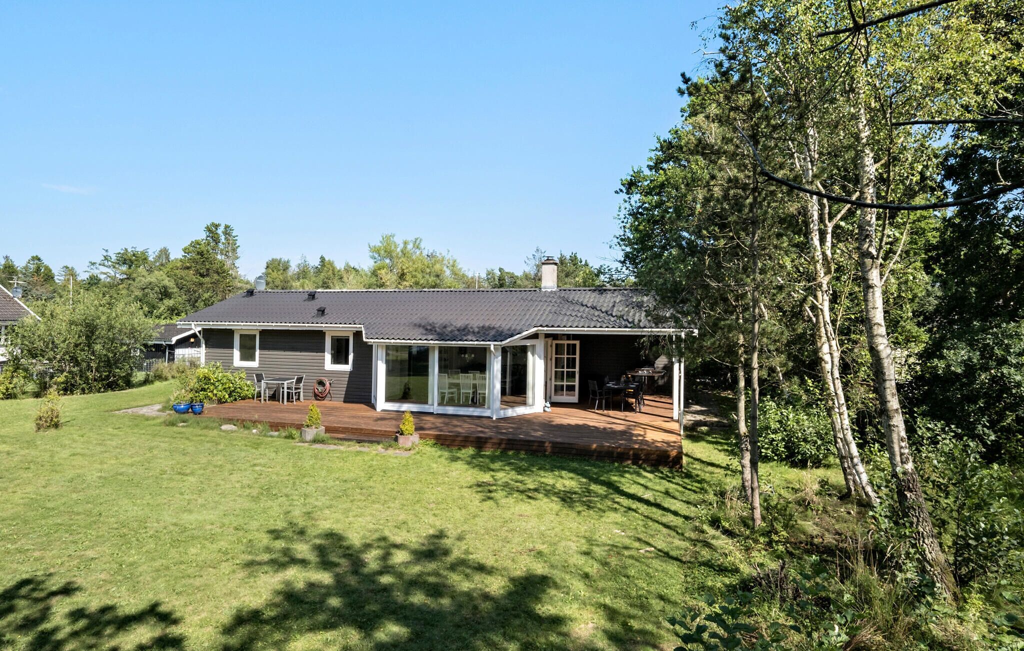 A house with a covered patio, a lawn, and trees in the background.