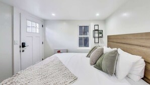 A bedroom with a bed, a door, a window, and a wall-mounted shelf.
