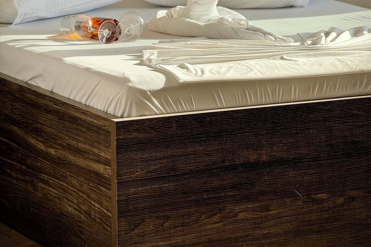 A neatly made bed with white linens, a folded towel, and a glass bottle on the bed.