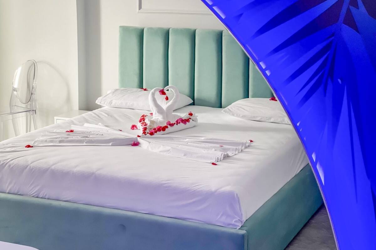A neatly made bed with white linens, a teal headboard, and decorative swan pillows.