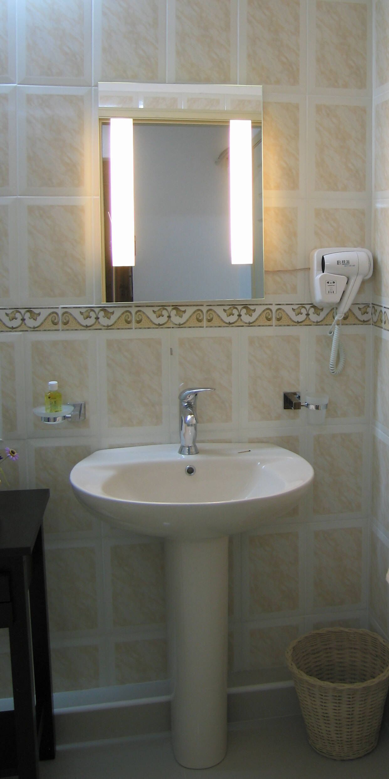 Une salle de bain avec un lavabo blanc, un miroir, un sèche-cheveux et un panier en osier.