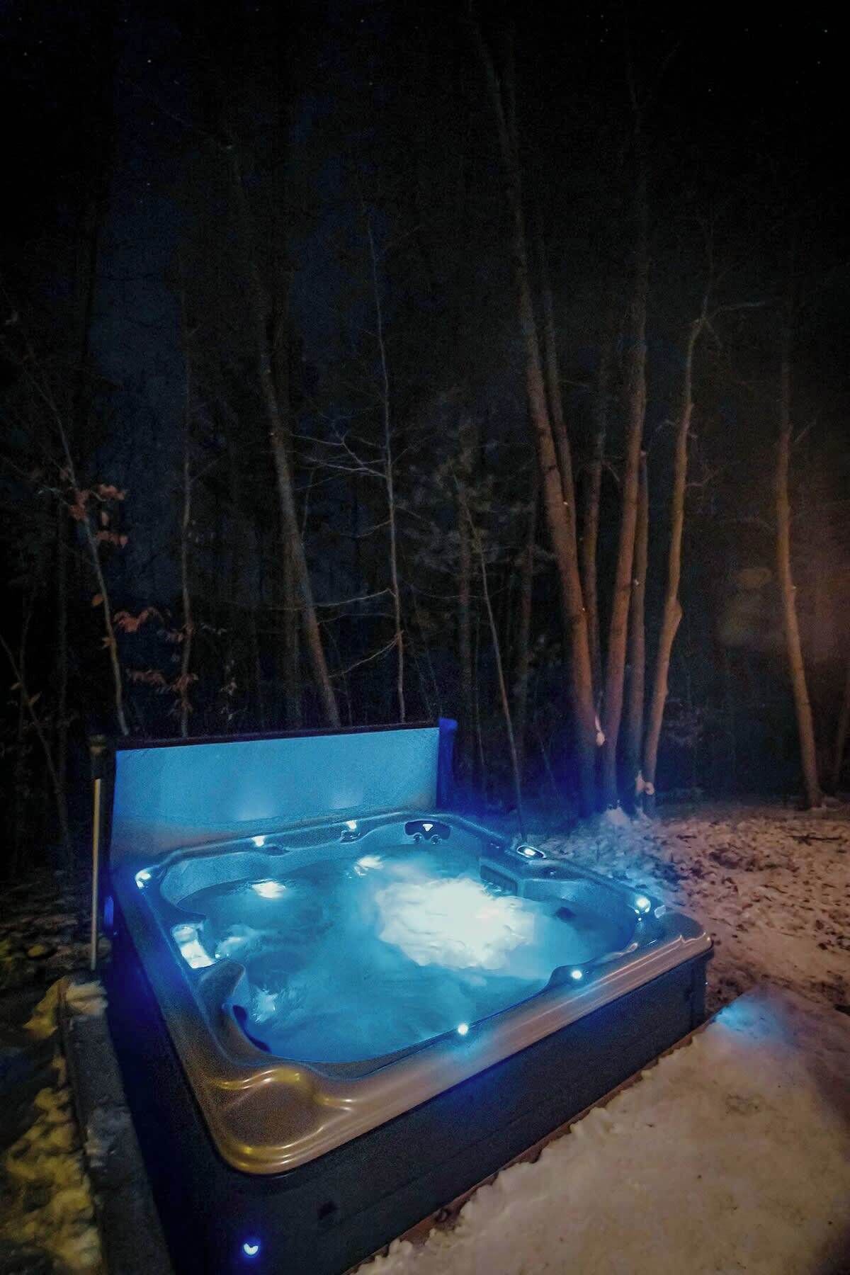 Un bain à remous installé à l’extérieur, la nuit, avec une forêt sombre en arrière-plan.