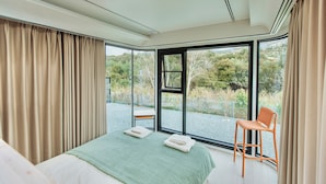 A bedroom with a large window, a bed, a chair, and a view of the outdoors. - Space shuttle around mountains - Geometry Park (Agios Theodoros)