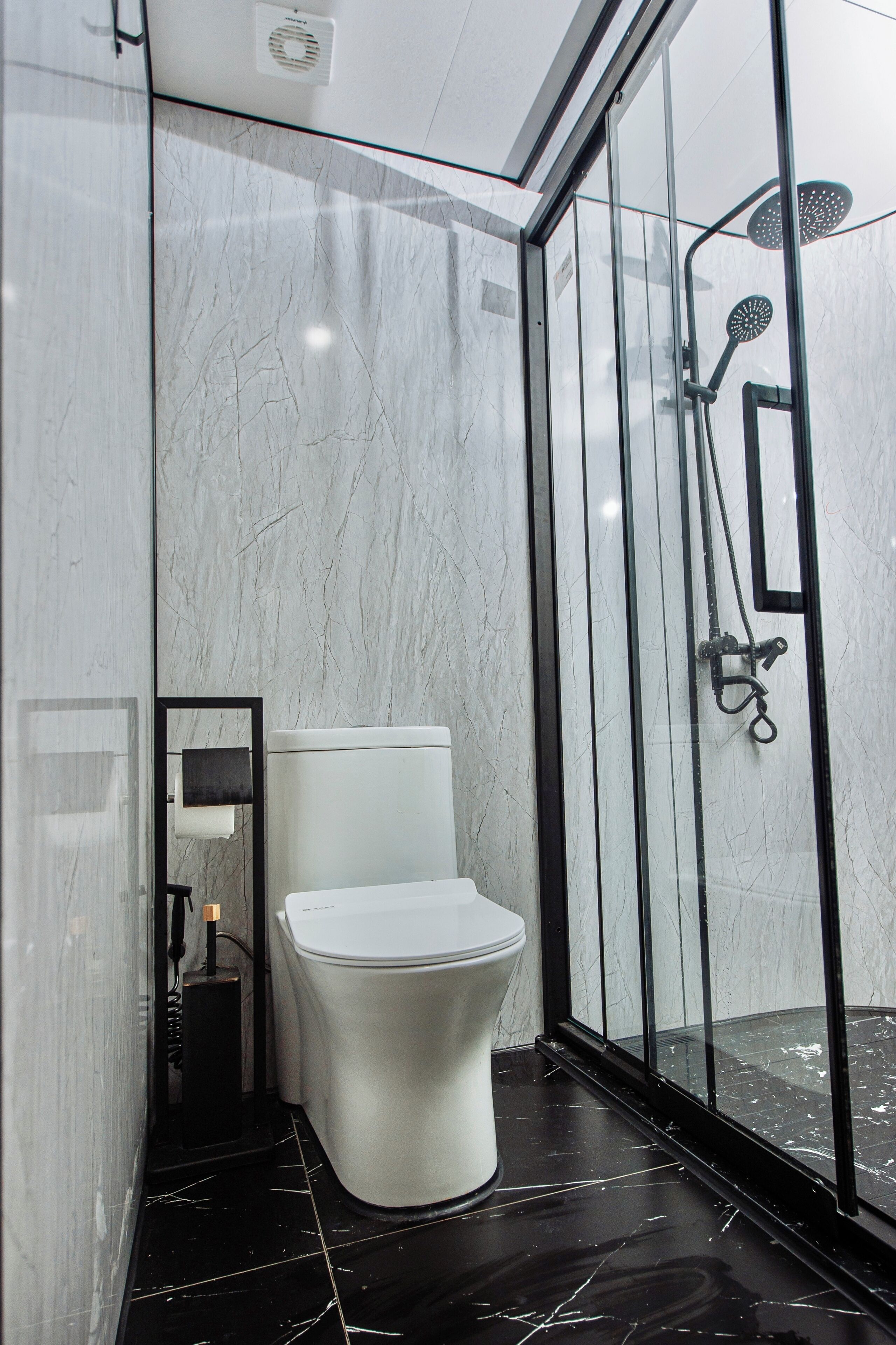 A modern bathroom with a toilet, a glass shower enclosure, and a marble floor.