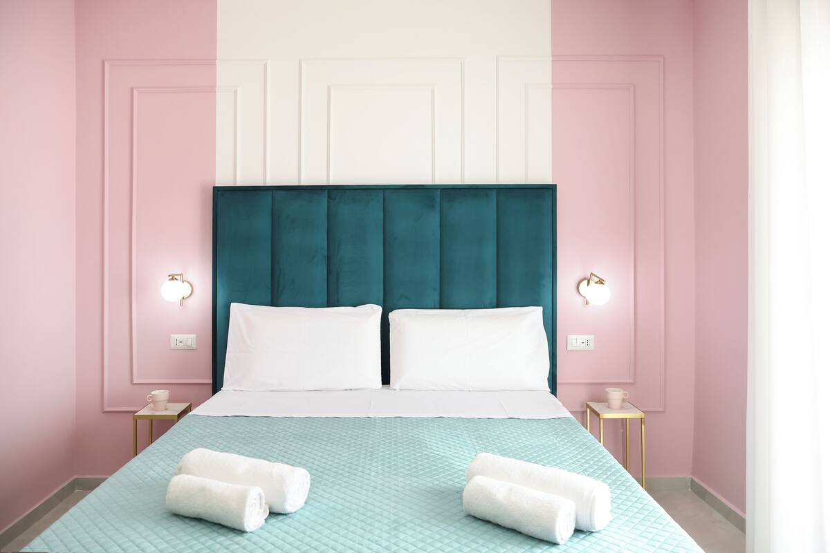 A neatly made bed with a teal headboard, white pillows, and a teal quilted bedspread. There are two bedside tables with lamps and a small table with a cup.
