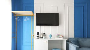 A room with a blue and white color scheme, a mounted television, a white desk with a coffee machine, and a blue chair. - Gresy Boutique Apartment (Naples)