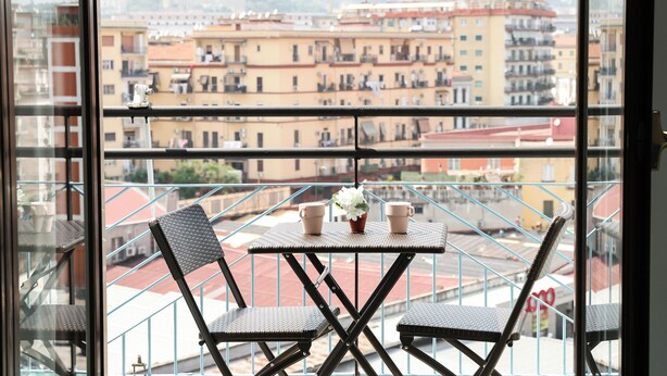A balcony with a table and chairs, a view of buildings, and a railing. - Gresy Boutique Apartment (Naples)