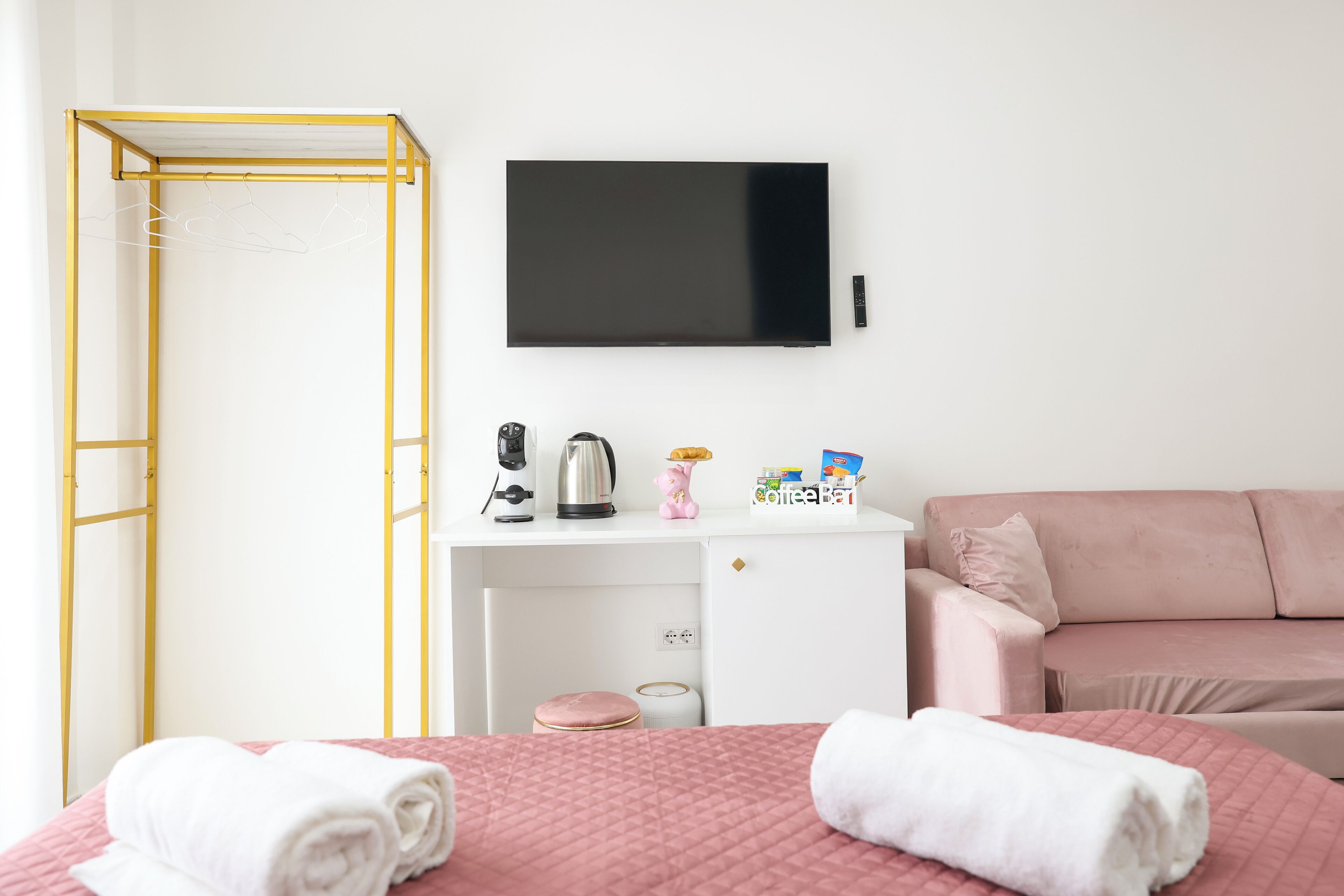 A hotel room with a bed, a desk with a TV, a coffee station, and a pink sofa.