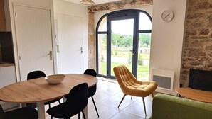 Een eethoek met een ronde houten tafel, zwarte stoelen, een gele fauteuil en een groene bank.