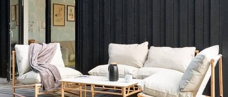 Een moderne buiten zithoek met een witte bank, een stoel en een tafel, voor een donkere muur met kunstwerken.